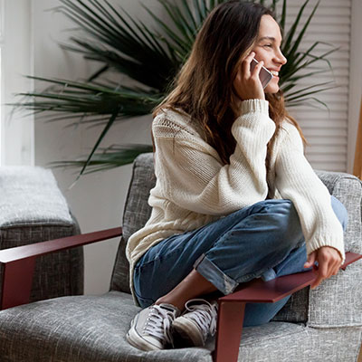 woman curled up on a chair speaking on a cell phone